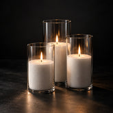 Three lit sand candles in clear glass cylinders on a dark background