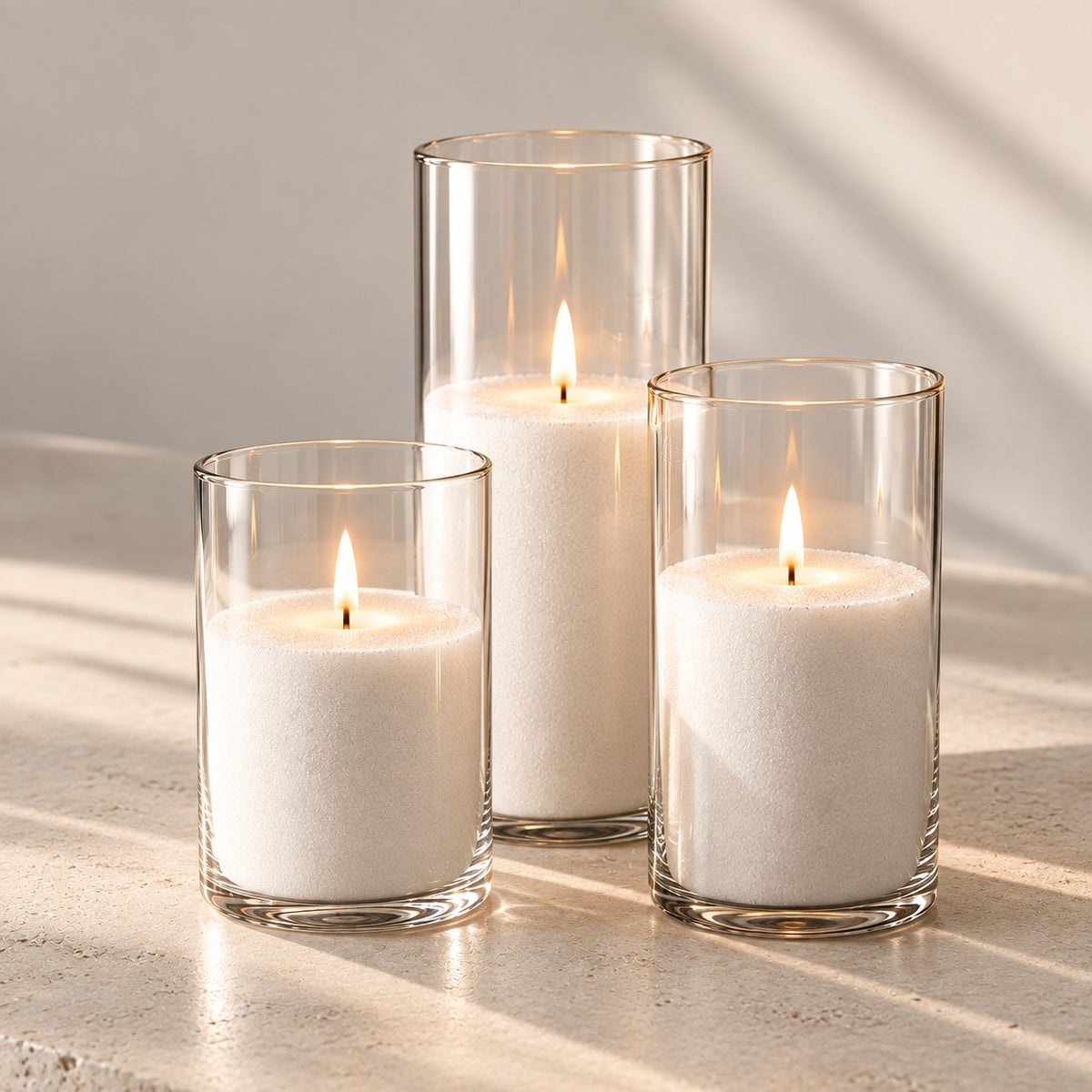 Three lit sand candles in clear glass cylinders in soft window light