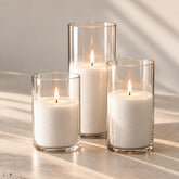 Three lit sand candles in clear glass cylinders in soft window light