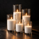 Five lit sand candles of different heights in clear glass cylinders on a dark background
