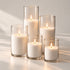 Five lit sand candles of different heights in clear glass cylinders in soft window light